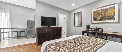 A hotel room with a bed, a desk, a chair, a television, and a kitchenette.