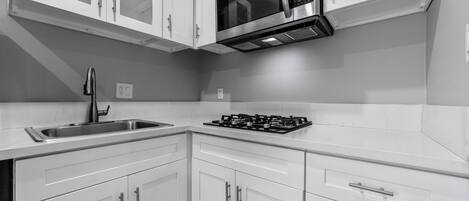 A modern kitchen with white cabinets, a stainless steel sink, a microwave, and a gas stove.