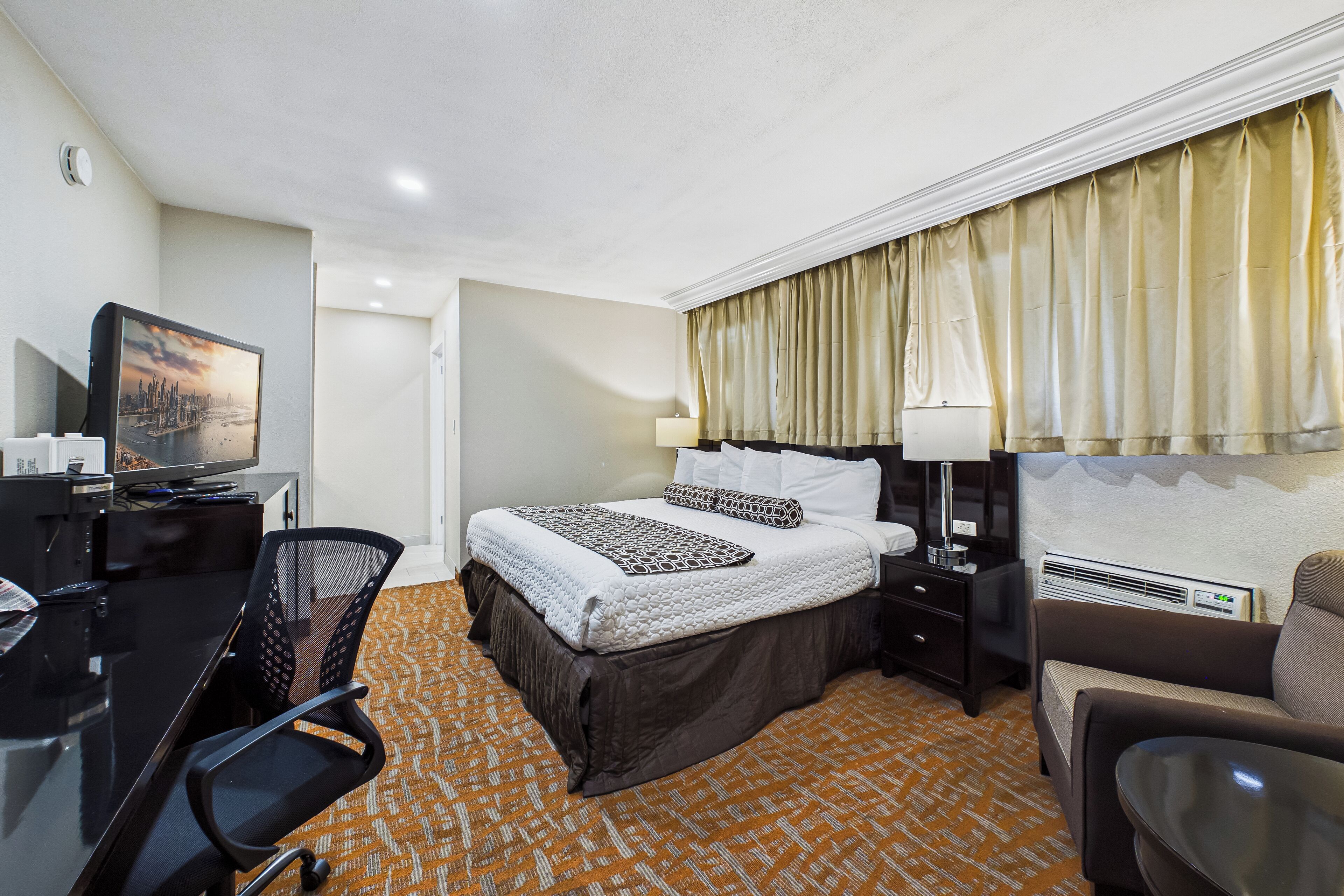 A hotel room with a bed, desk, chair, and a television.
