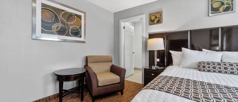 A hotel room with a bed, a chair, a nightstand, and two framed abstract paintings on the wall.