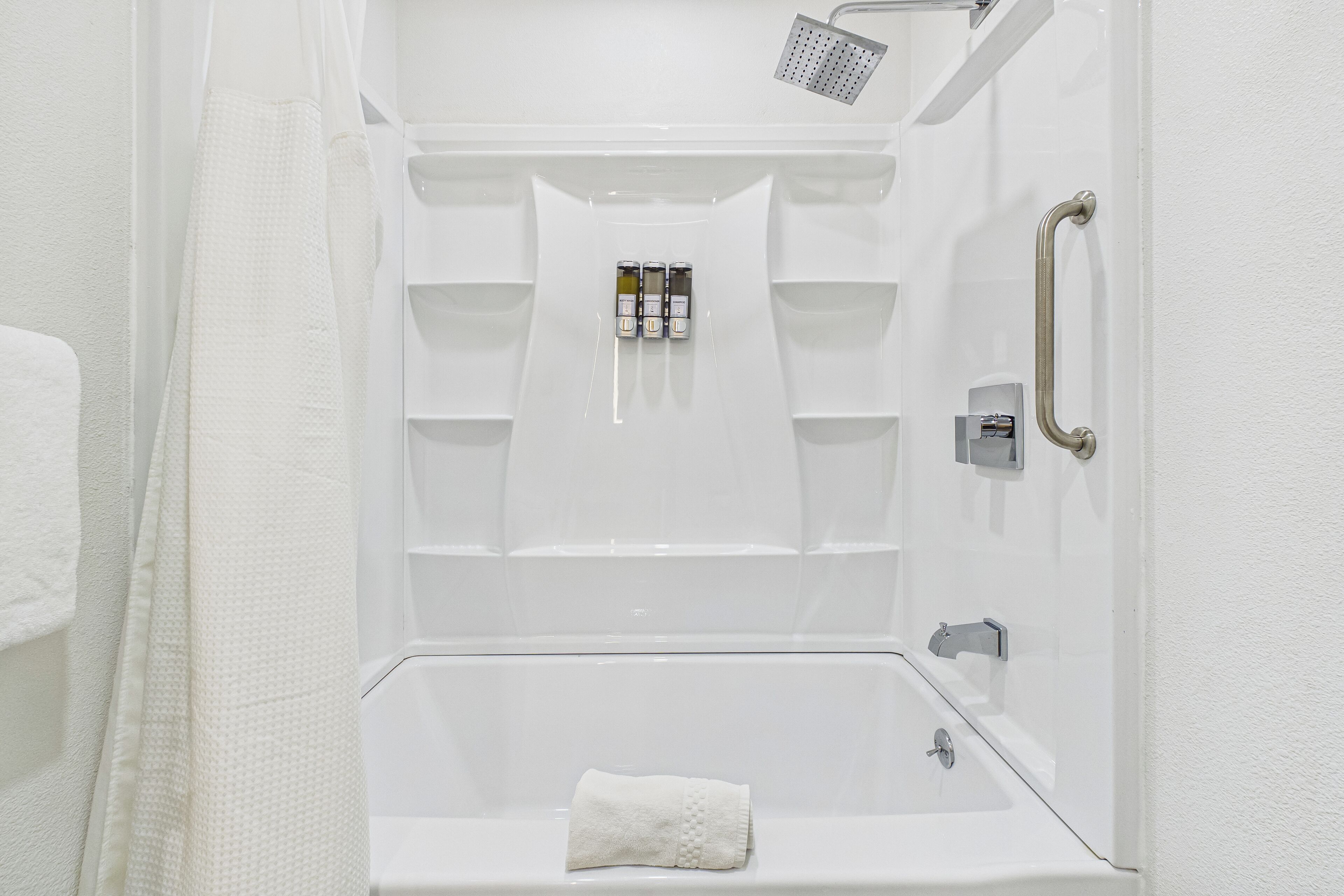 Cabina de ducha blanca con cabezal de ducha de mano, una toalla y un estante con artículos de aseo.