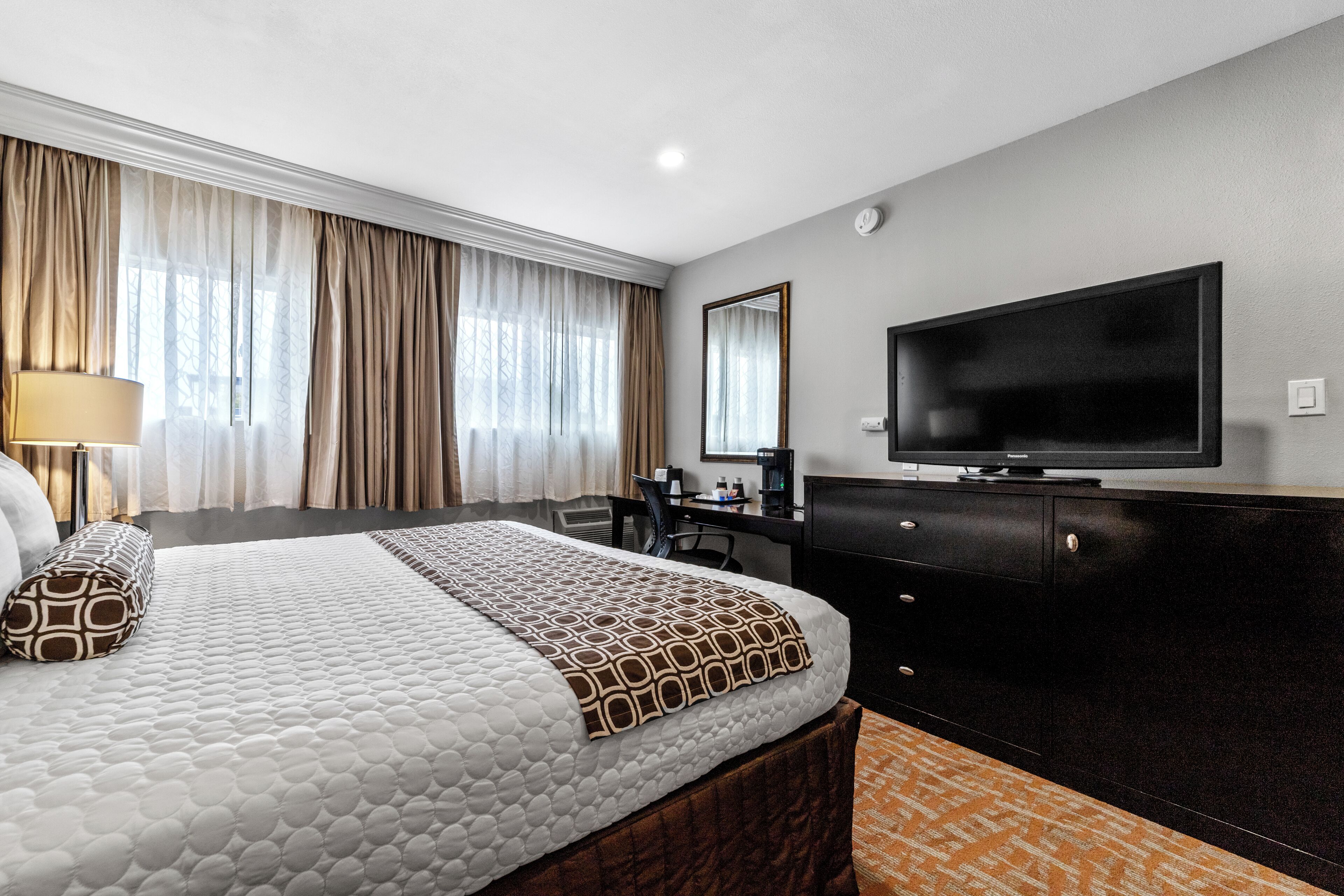 A hotel room with a large bed, a desk, a television, and a window with curtains.