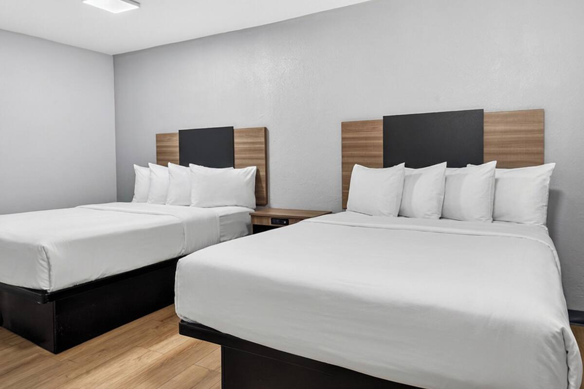 A hotel room with two beds, each with a wooden headboard, white bedding, and a nightstand between them.