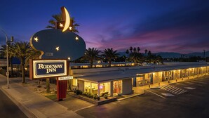 A motel with a large illuminated sign, a parking lot, and a row of rooms with visible windows. - Rodeway Inn Las Vegas Fremont Street (Las Vegas)