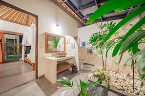 Ein Badezimmer mit einem großen Spiegel, einem Waschbecken mit Becken aus Stein und einer kleinen Pflanzenecke mit Kieselsteinen.