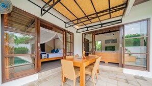 Una habitación moderna con un gran ventanal corredero que da a un balcón, una mesa de comedor de madera con sillas y una cama con dosel.