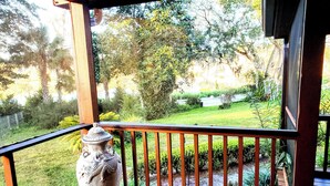 Una terraza de madera con barandilla, un gran jarrón decorativo y vistas a un jardín cuidado con diversas plantas y un pequeño estanque.