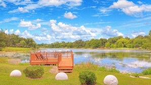 Una terraza de madera con asientos que da a un lago tranquilo, rodeada de exuberante vegetación y árboles.