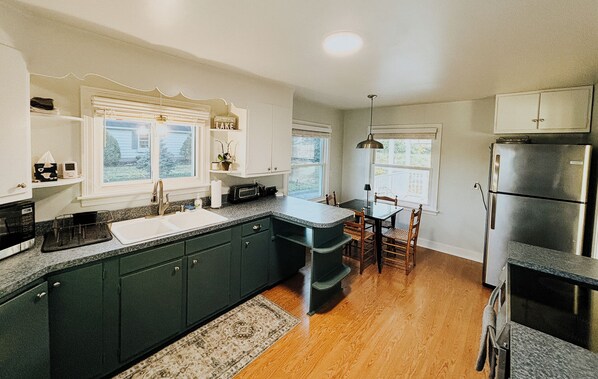 A kitchen with dark green cabinets, a granite countertop, a built-in island, a refrigerator, and a dining area with a table and chairs.