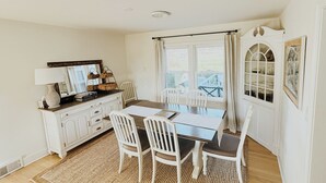 Un coin repas comprenant une table, des chaises, un meuble blanc, un miroir et une fenêtre avec des rideaux.