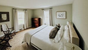Une chambre à coucher avec un grand lit, une commode en bois, un fauteuil à bascule et un tableau encadré au mur.