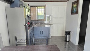 Una cocina moderna con armarios grises, un lavamanos de acero inoxidable y una ventana con rejas. Hay un comedor con una mesa de madera y sillas de metal.