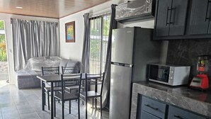 Cocina compacta con refrigerador, microondas y licuadora sobre la encimera. Hay un comedor con sillas y una mesa.