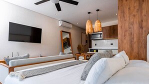 A modern bedroom with a large bed, a TV mounted on the wall, and a kitchenette area.