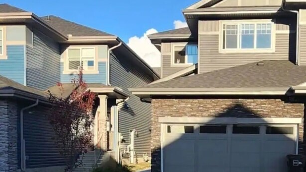 A residential street with houses, a clear sky, and a driveway leading to a garage.