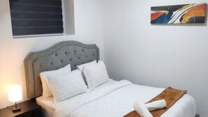 A bedroom with a bed, a nightstand, a window, and a painting on the wall.