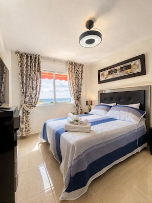Um quarto com uma cama, cortinas, uma mesa de cabeceira, um abajur e uma luminária no teto.