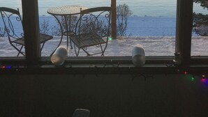 Huone, josta avautuu näkymä järvelle auringonlaskun aikaan. Huoneessa on ikkunan vieressä pöytä ja tuolit.