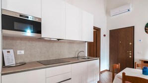 A modern kitchen with white cabinets, a stainless steel oven, and a sink. There is a dining table with chairs and a blue vase.