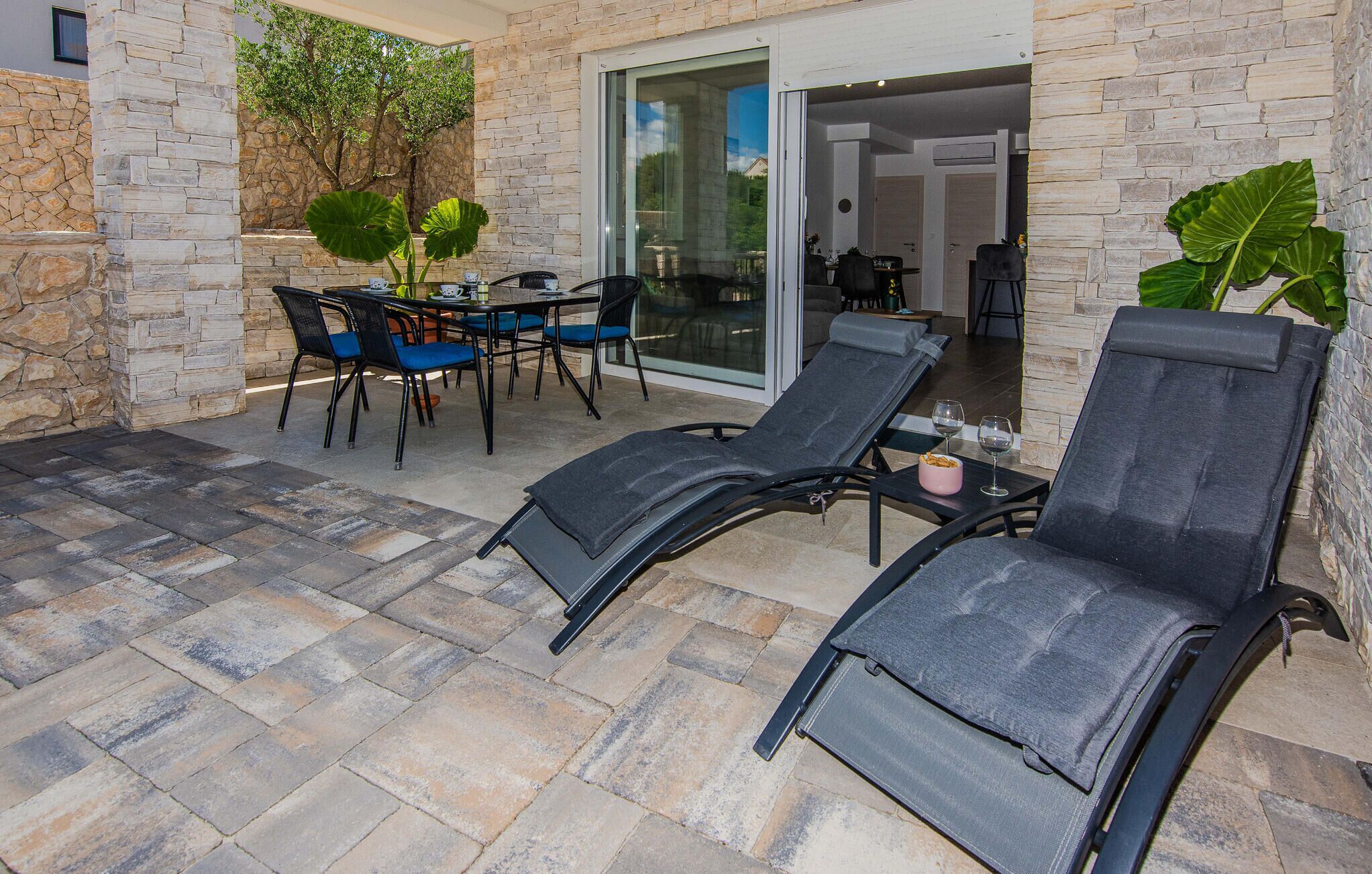 A patio area with stone flooring, a table with chairs, and two lounge chairs.