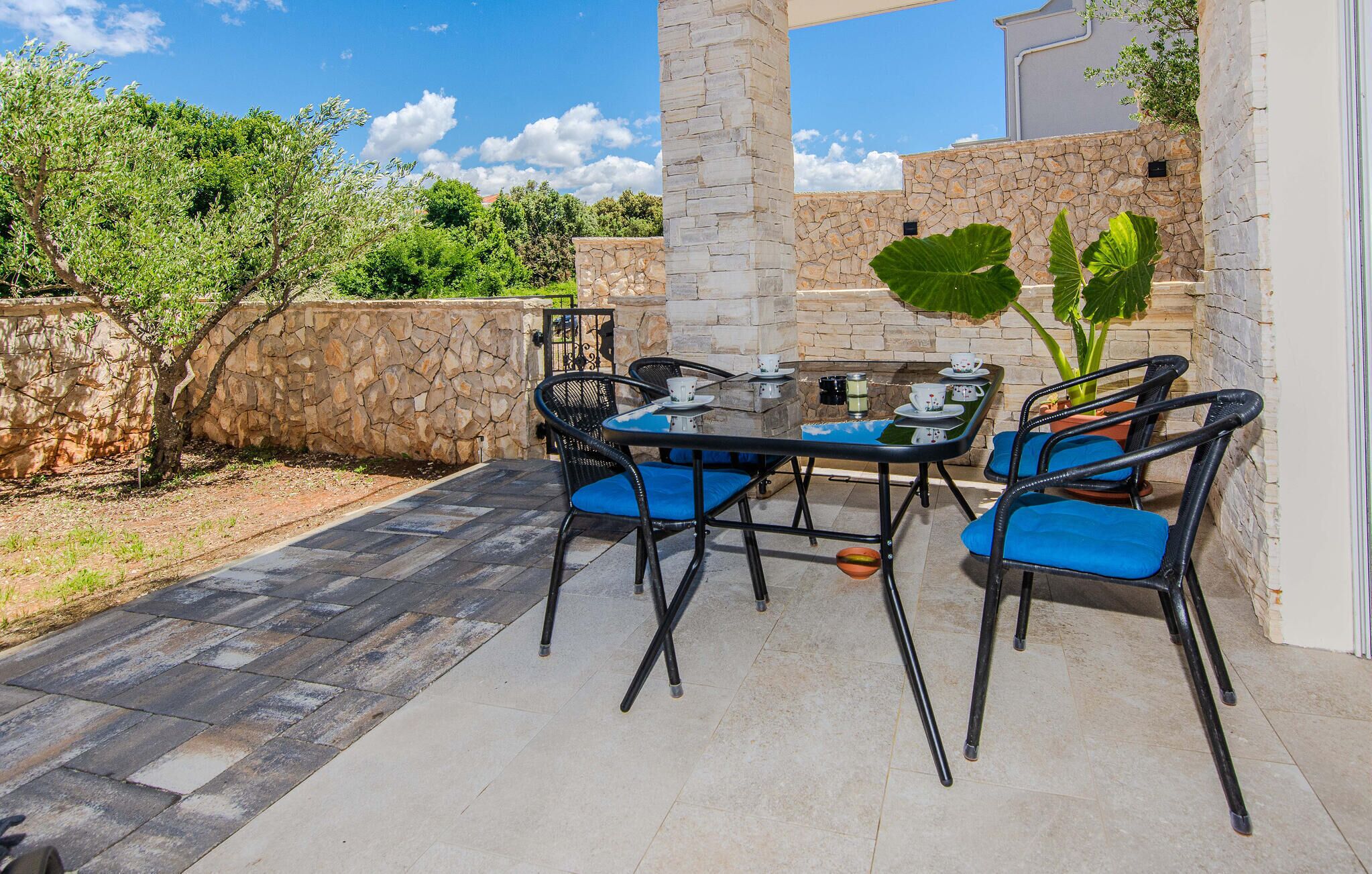 An outdoor patio with a stone wall, a table with chairs, and a view of trees and sky.