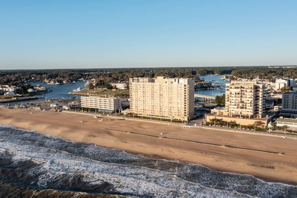 A coastal hotel with multiple high-rise buildings, a beach in the foreground, and a marina in the background.
