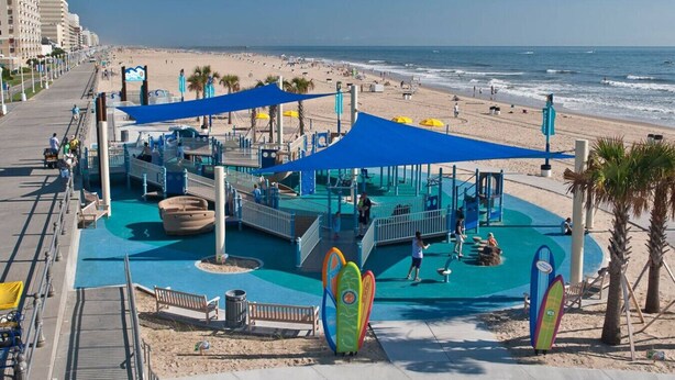 A beachside water park with a blue pool area, palm trees, and a sandy beach in the background. - Oceanfront Condo, Heated Pool, Fitness Center (Virginia Beach)
