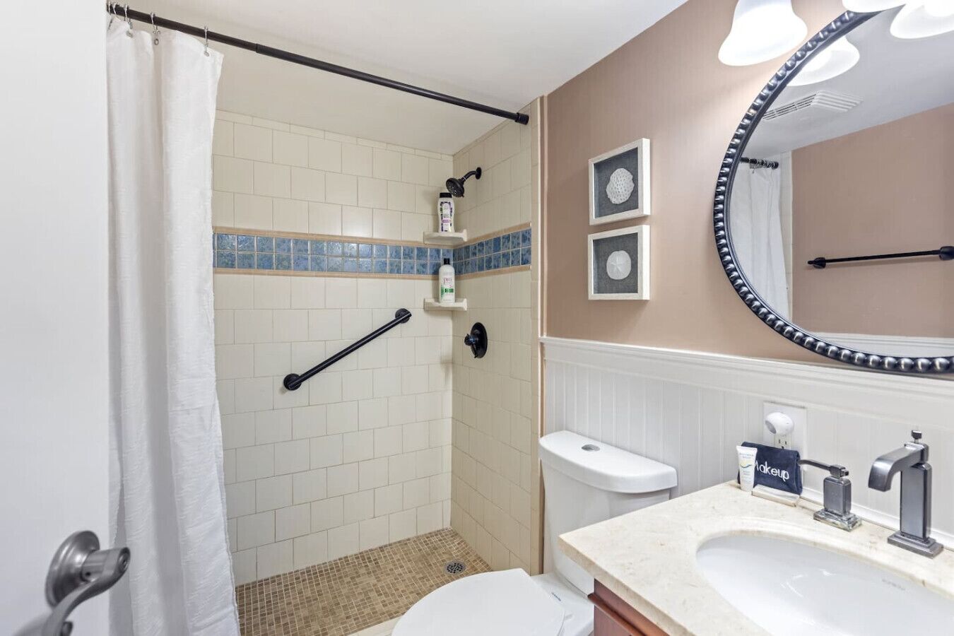 Une salle de bain équipée d’une douche, de toilettes, d’un lavabo et d’un miroir agrémenté d’un cadre décoratif.