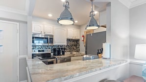 A modern kitchen with white cabinets, a marble countertop, stainless steel appliances, and pendant lighting. - Oceanfront Condo, Heated Pool, Fitness Center (Virginia Beach)