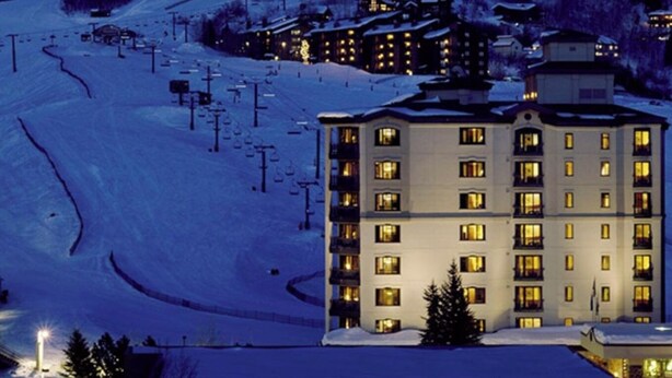 Estación de esquí cubierta de nieve de noche, con edificios iluminados y un telesilla.