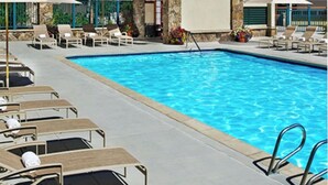 Un área de piscina con sillones de descanso y sombrillas, rodeada de un paisaje montañoso.