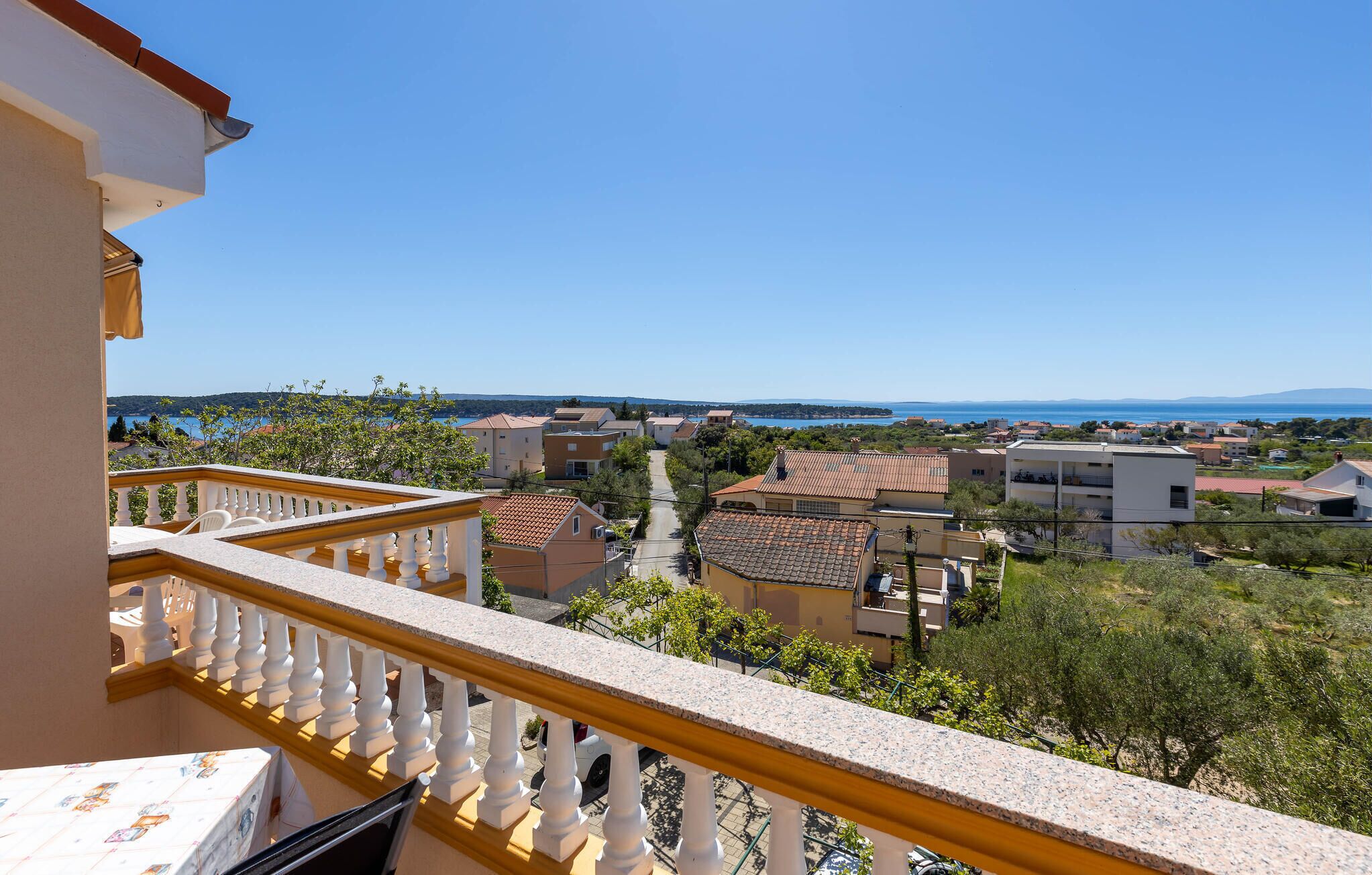 A balcony with a view of a residential area, featuring houses with red-tiled roofs and a clear blue sky.