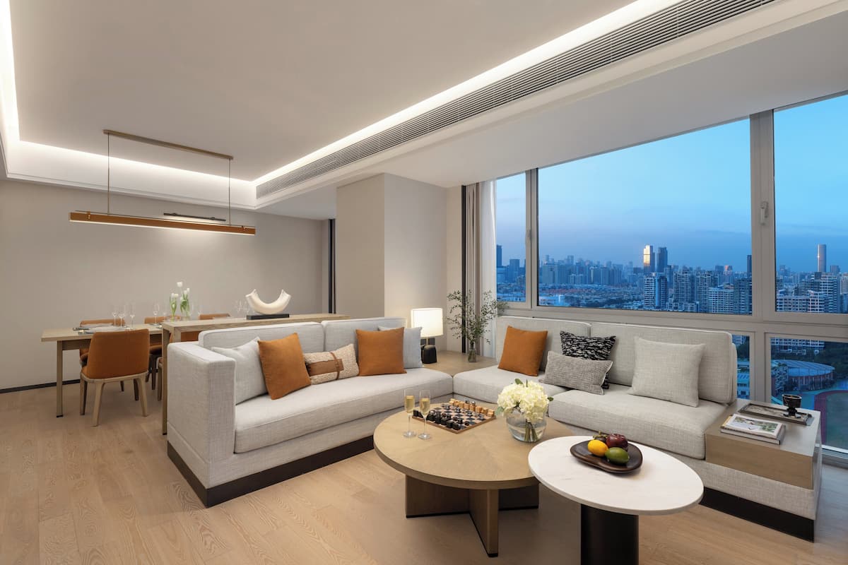 A modern living room with a sectional sofa, a dining area, and a large window with a city view.