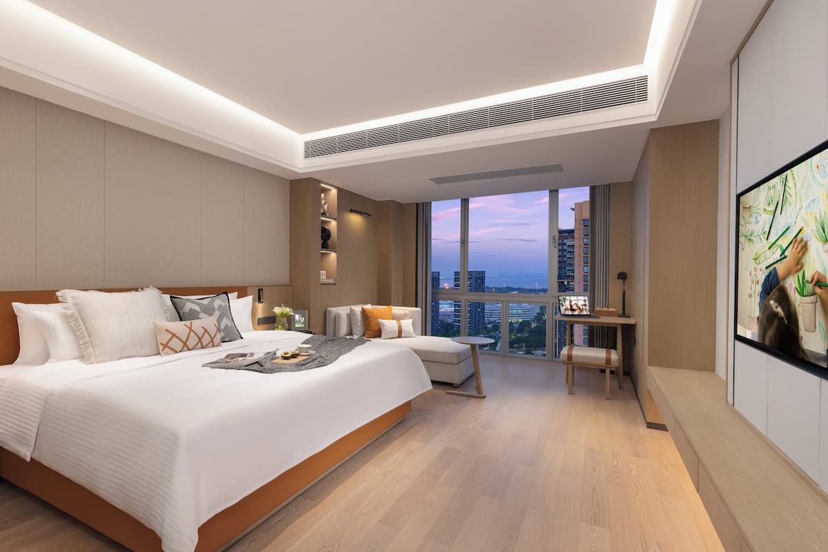 A modern hotel room with a large bed, a desk, and a view of the city.
