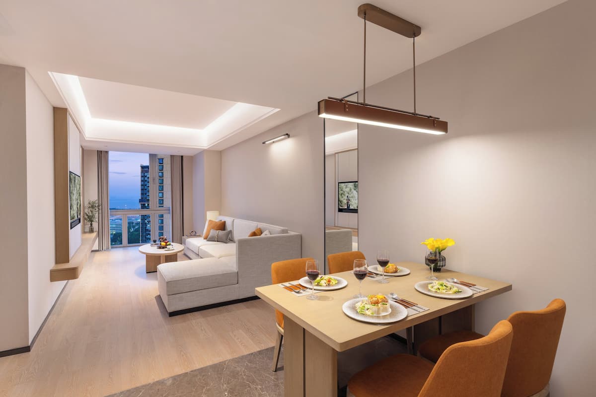 A modern living room with a dining area, featuring a sofa, a dining table with chairs, and a large window with a view of the city.