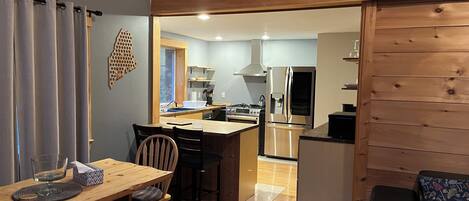 Una cocina compacta con una isla central, un comedor con mesa y sillas de madera, y una zona de estar acogedora con un banco acolchado.
