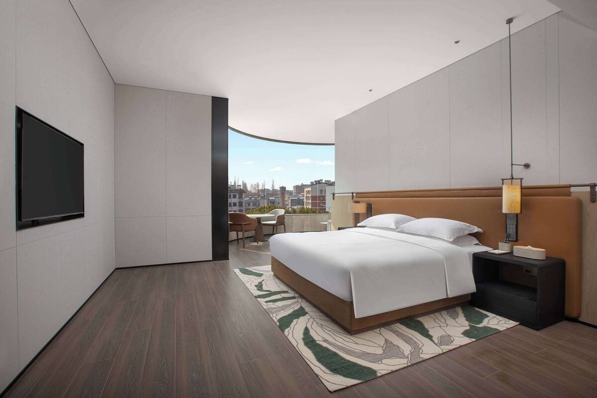 Ein modernes Hotelzimmer mit einem großen Bett, einem Flachbildfernseher, einem Schreibtisch und Blick auf die Stadt.