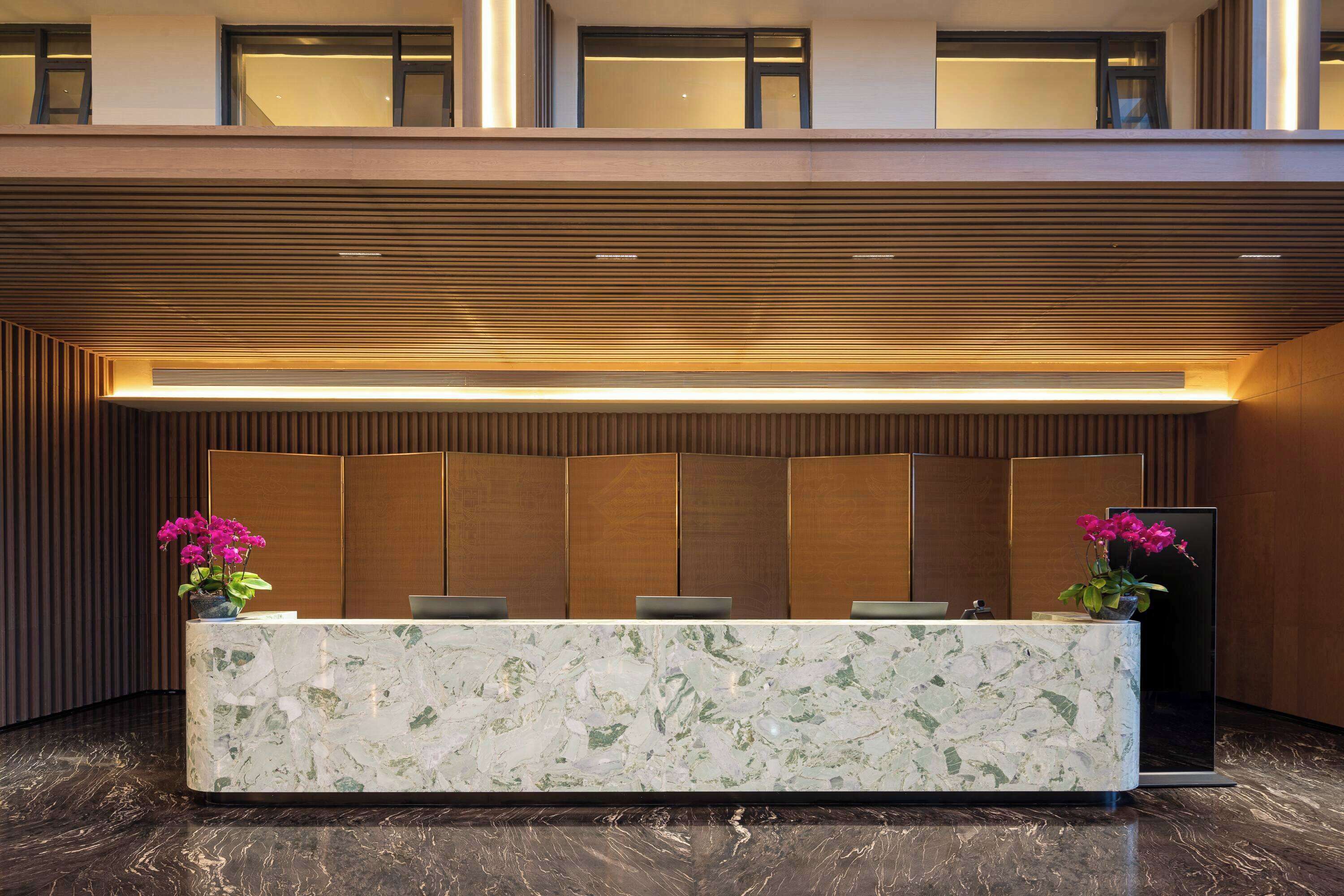 A reception desk with a marble top, two chairs, and a potted plant.