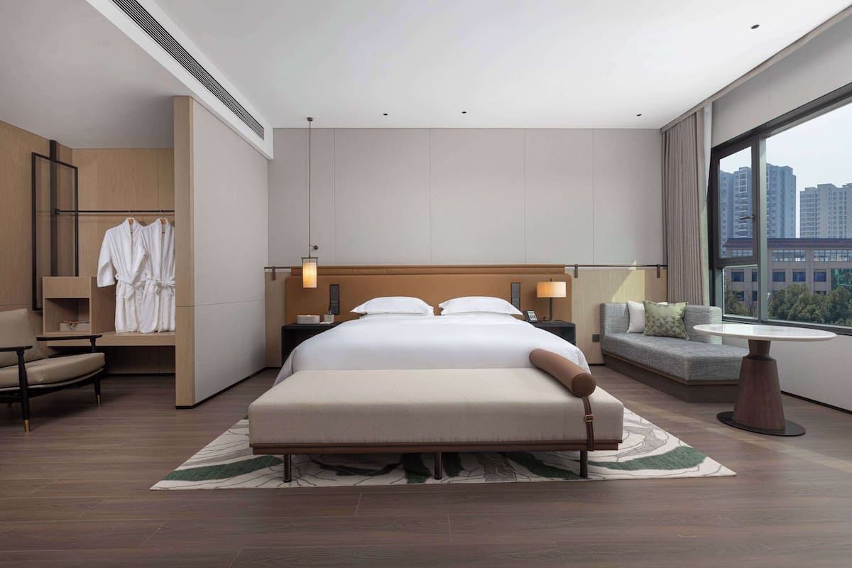 Ein modernes Hotelzimmer mit einem großen Bett, einer Sitzecke, einem kleinen Tisch und Blick auf die Stadt.