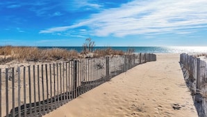 A sandy beach path with a wooden fence and sparse vegetation.
