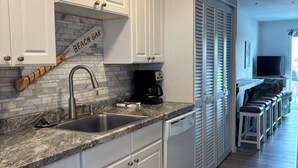 A modern kitchen with white cabinetry, a granite countertop, a coffee maker, and a sink.
