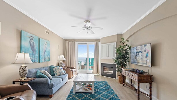 A living room with a sofa, coffee table, and a television. There is a ceiling fan, a fireplace, and a window with curtains.