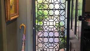 Eine Tür mit einem geometrischen Metallgitter, einem hölzernen Türrahmen und einem kleinen Regenschirm, der an der Wand lehnt.