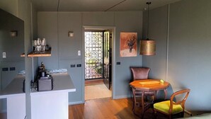 Eine moderne Küche mit weißer Arbeitsplatte, einer Kaffeemaschine und einer dekorativen Vase. Ein Essbereich mit Holztisch und Stühlen lädt zum Verweilen ein, und ein großes Fenster bietet einen Blick ins Freie.