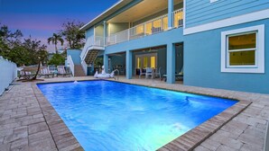 A swimming pool with a brick border, a covered patio area, and a two-story building with a balcony. - Pool Home with Beach Access - Southern Comfort - Roelens (Fort Myers Beach)