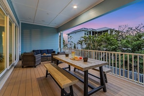 Um deck de madeira com mesa e bancos, ladeado por um corrimão, com vista para uma área residencial com casas e vegetação.