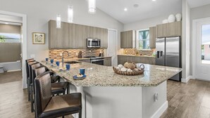A modern kitchen with a central island, stainless steel appliances, and a dining area with leather chairs. - Pool Home with Beach Access - Southern Comfort - Roelens (Fort Myers Beach)