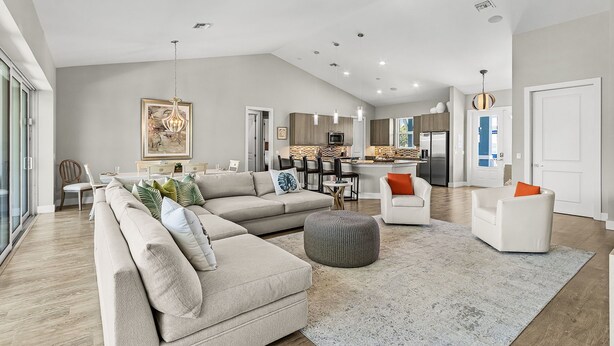 A spacious living room with a large sectional sofa, ottoman, and a dining area with a kitchen in the background. - Pool Home with Beach Access - Southern Comfort - Roelens (Fort Myers Beach)
