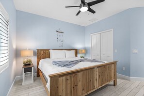 A bedroom with a wooden bed, two bedside tables with lamps, a ceiling fan, and a white door.
