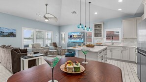 Una cocina moderna con armarios blancos, un refrigerador de acero inoxidable y un comedor con una mesa de madera y dos vasos de martini.